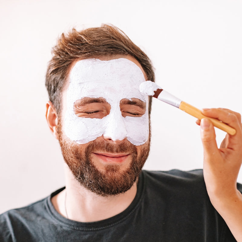 Man applying a white facial mask to his face with a brush.