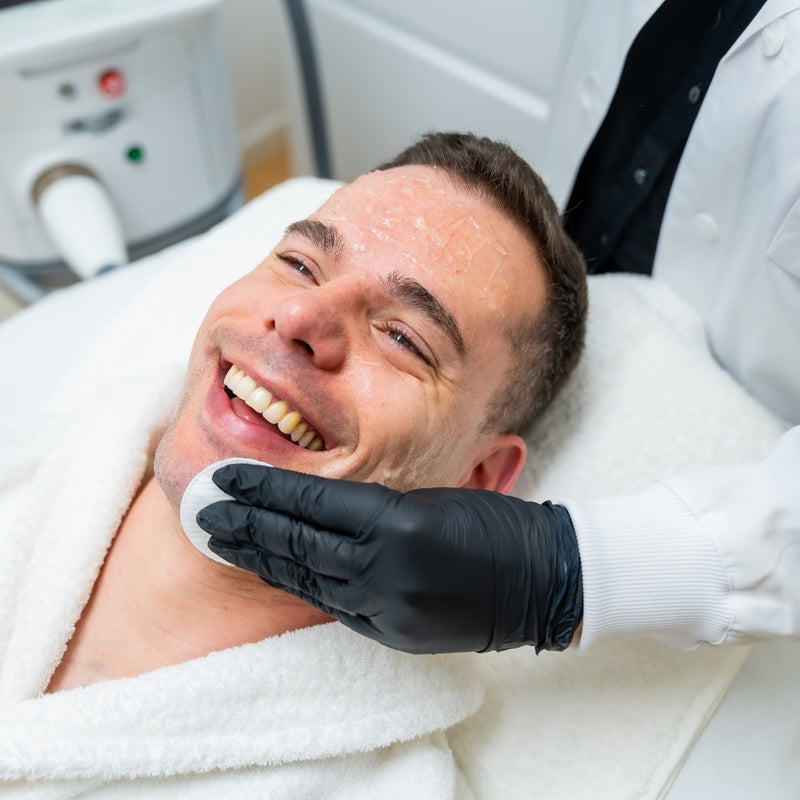 Man receiving a facial treatment with a professional in a clinical setting.
